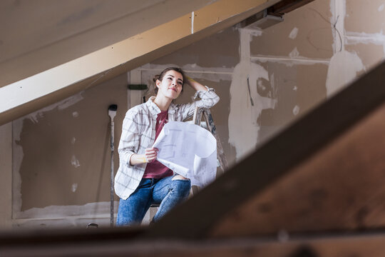 Contemplative woman holding blueprint at home