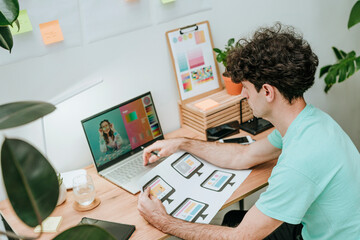 Web designer holding document and working on laptop at desk in office