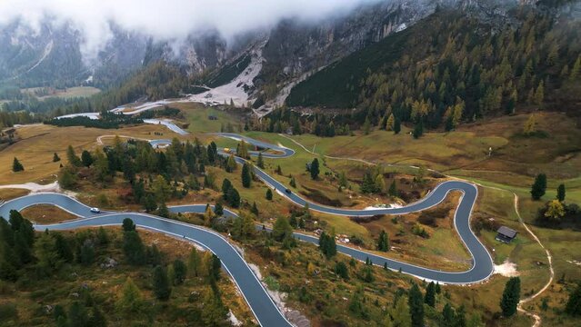 Aerial drone view of a winding road surrounded by autumn trees with mountains in the background in Dolomites, Italy