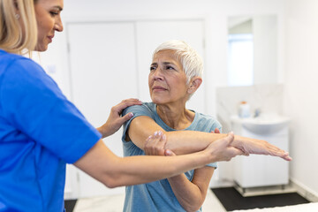 Caregiver helping contented senior woman exercise at clinic. Rehab for elder, senior medical care....