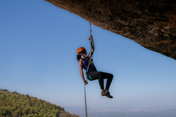Image of a determined and brave girl climbing an imposing rock face. With an expression of...