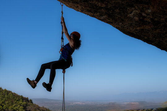 Image of a determined and brave girl climbing an imposing rock face. With an expression of concentration on her face, she holds on to the rope with determination.