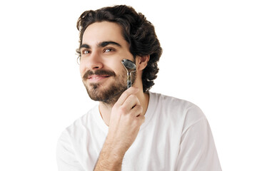 Portrait of man moves smoothly over skin of his face with massage roller against white studio...