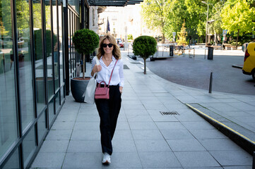 Attractive blond haired woman wearing white shirt and black pants and walking on the city