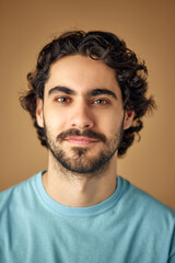 Close up portrait of handsome young man looking at camera against beige studio background. Bearded guy. Concept of natural beauty, youth, spa treatment, male health, selfcare, cosmetic. Ad