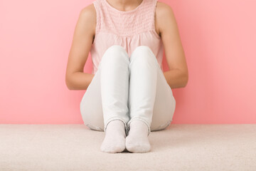 Alone girl in shirt, white jeans and socks sitting on light beige carpet at pink wall background....