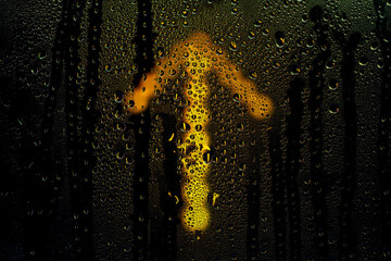 Glowing arrow sign pointing up behind wet glass. Raindrops on the window. Background on the theme...