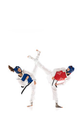 Full-length image of young competitive girls in dobok and helmet, practicing taekwondo, training isolated over white background. Concept of martial arts, combat sport, competition, action