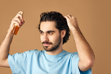 Hair repair treatment. Serious young man applying essential oil spray on his curly brown hair...