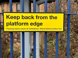 Yellow caution sign keep back from platform edge on a metal fence