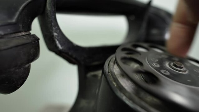 A person dials a number on a vintage telephone. Сalling with black retro phone. Man picks up handset on old phone and turns number plate of device. Close-up Dusty Retro Rotary Landline Phone