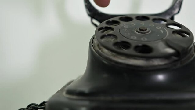 A person dials a number on a vintage telephone. Сalling with black retro phone. Man picks up handset on old phone and turns number plate of device. Close-up Dusty Retro Rotary Landline Phone