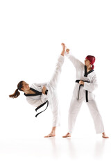 Young sportive girls in kimono and black belted practicing karate, judo, taekwondo stunts isolated over white background. Concept of martial arts, combat sport, competition, action