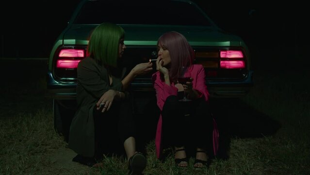 Girl couple with colored hair lighting a cigarette near the retro car outdoors