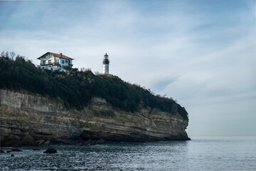 Fototapeta na wymiar Falésia ou elevação rochosa com um farol e uma casa lá no alto junto à praia de Petite chambre d'amour em Biarritz no País Basco, França 