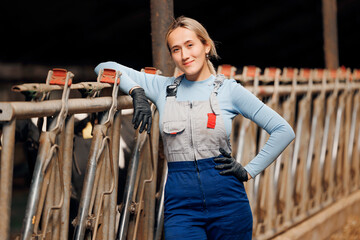 Happy smiling young woman farmer in bard of cows on dairy farm. Agriculture industry, farming...