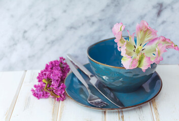 Spring Table Setting with Blue Cutlery and Lilac Flowers on a Wooden Background.Floral Table Decor