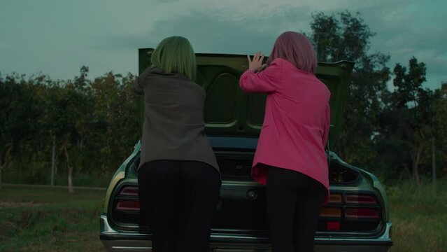 Green hair girl and her girlfriend with pink hair opening the car's trunk outdoors