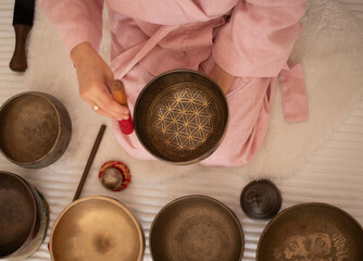 Fototapeta premium Woman in pink clothes hold sound metal bowl and make music in spa salon. Yoga for health, relaxation and meditation body, practice for forgiveness and spiritual harmony.