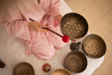 Woman in pink clothes hold sound metal bowl and make music in spa salon. Yoga for health, relaxation and meditation body, practice for forgiveness and spiritual harmony.