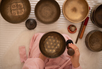 Woman in pink clothes hold sound metal bowl and make music in spa salon. Yoga for health, relaxation and meditation body, practice for forgiveness and spiritual harmony.