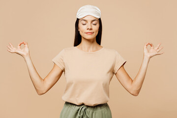 Young Latin woman wears pyjamas jam sleep eye mask rest relax at home hold hands in yoga om aum...