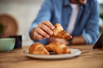 Closeup of a male hand holding a brown crispy croissant.