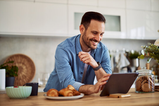 A happy homemaker searches for a recipe on a tablet while leaning on a kitchen counter.