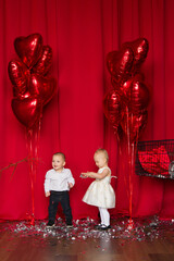 Little cute girl and boy in a red heart with balloons. Valentine's Day celebration. love. Two angels on a red curtains