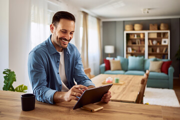 A smiling male freelancer using his tablet for work sitting at a table next to a cup of coffee.