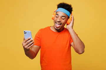 Young fitness trainer sporty man sportsman wear orange t-shirt listen music in headphones use...