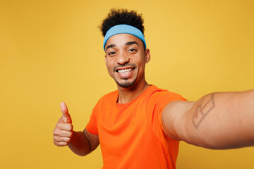 Close up young fitness trainer sporty man sportsman wear orange t-shirt spend time in home gym do selfie shot on mobile cell phone isolated on plain yellow background. Workout sport fit abs concept.