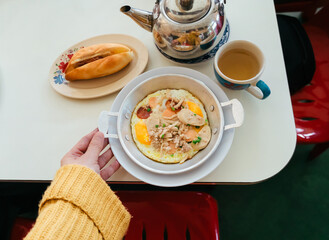 Top view of Hand holding Panned Eggs Thai style or Pan Fried Eggs with ham, sausages, and vegetable toppings is delicious Thai food. Pan fried egg and Vietnamese sandwich and Chinese tea.