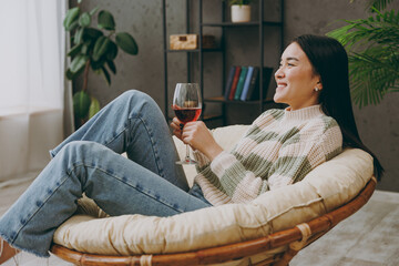 Side view young smiling fun happy woman she wearing casual clothes drink red wine sits on armchair...