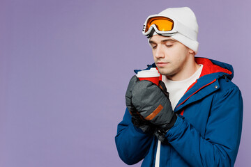 Skier man wear warm blue windbreaker jacket ski goggles mask hat mittens hold takeaway delivery cup coffee to go spend extreme weekend winter season in mountains isolated on plain purple background.