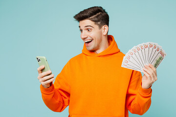 Young man wears orange hoody casual clothes hold in hand fan of cash money in dollar banknotes use...