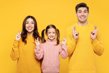 Young happy parents mom dad with child kid girl 7-8 years old wear pink knitted sweater casual clothes wait special moment keep fingers crossed isolated on plain yellow background Family day concept. - obrazy, fototapety, plakaty