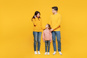 Full body young parent mom dad with child kid girl 7-8 years old wear pink sweater casual clothes stand with little daughter look to each other isolated on plain yellow background. Family day concept