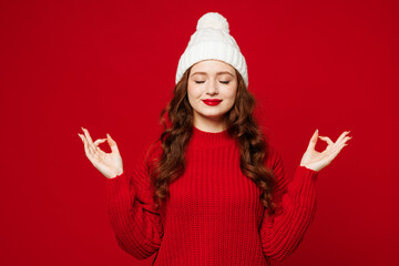 Young spiritual woman wears knitted sweater white hat casual clothes hold spread hands in yoga om...