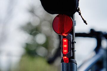 Glowing bicycle taillight. Red stop light for cyclist safety. Rear led light on bike - obrazy, fototapety, plakaty