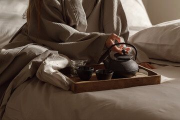 Black cast iron tea pot with herbal tea set up on wood tray on the bed. Traditional Asian Tea Set -...