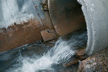 The river is polluted by industrial waste from a drainpipe that dumps sewage into the water, harming the natural ecosystem.