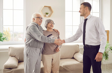 Portrait of happy cheerful senior couple standing in the living room at home shaking hands and...
