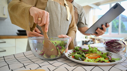 Cropped shot of senior woman reading recipe on digital tablet, cooking healthy vegetable salad in kitchen