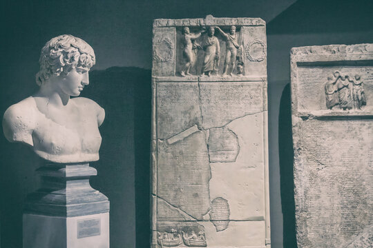 Antinous statue in exhibition, some greek stellas nearby. Toning. Antinous is a young man, favorite and lover of Roman emperor Hadrian. National Archaeological Museum, Athens, Greece. Dec. 11, 2018