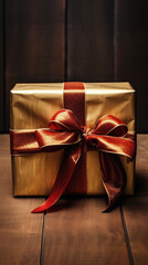 Golden gift box with red ribbon bow on wooden background, close up.