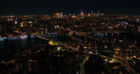 Iconic New York City Nightlife Landscape Over East River with Skyscrapers, Manhattan and Brooklyn Bridges, Cars and Ferry Boats. Cinematic Night Urban Skyline with Office Buildings with Lights