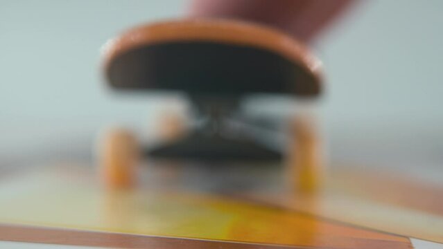 A close-up macro detailed shot of a mini skateboard, tiny white wheels, riding fingerboard, finger slide back and forward in front of the camera, professional lighting, static cinematic 4K video