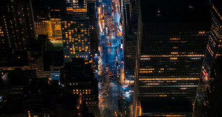 Night Aerial Photo of New York City with Skyscraper Spires and Straight Busy Streets with Cars and Yellow Taxi Vehicles. Top Down Helicopter View of Office Buildings in a Big Urban Center