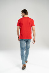 Fototapeta na wymiar Man in jeans and red t-shirt is walking. Rear view. Full length studio shot isolated on white